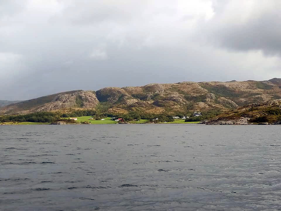 Farms and green fields at the foot on a mountain with the sea in front.