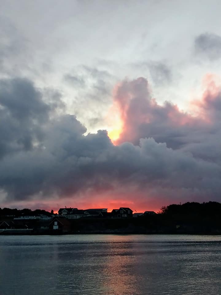 Silhouette of houses in the distance and big dramatic clouds with a red sunset shining behind them. 