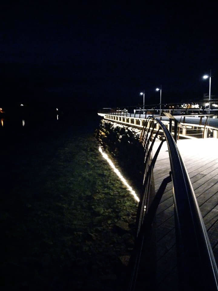 A pier at night time with lights reflecting in the water.