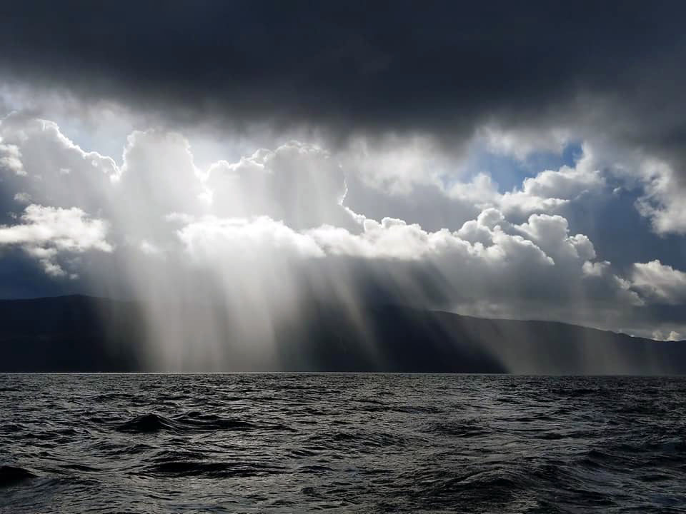 The sea and a mountain in the distance where the rain is pouring down.