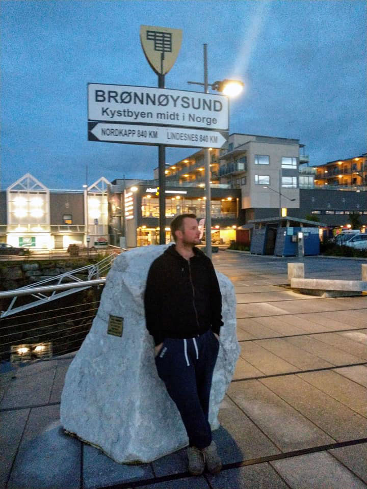 V leaning against Brønnøysund sign. 