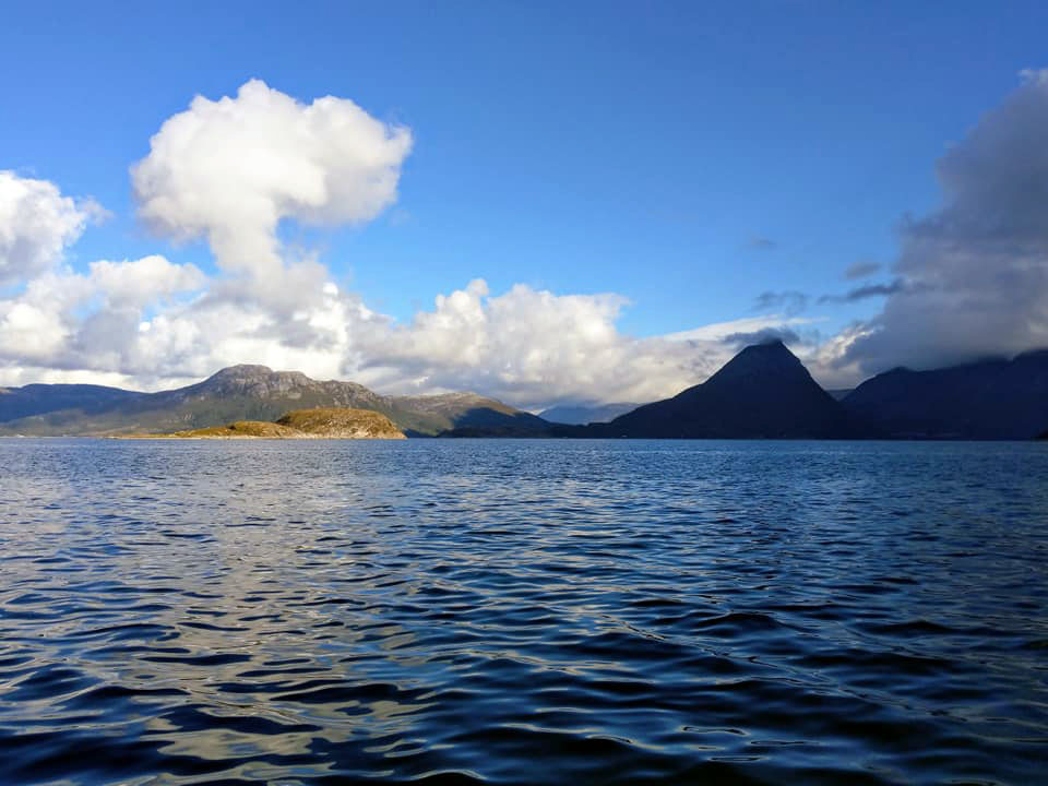 Sea with mountains way in the distance and a big clouds rising up shaped almost like a mushroom.