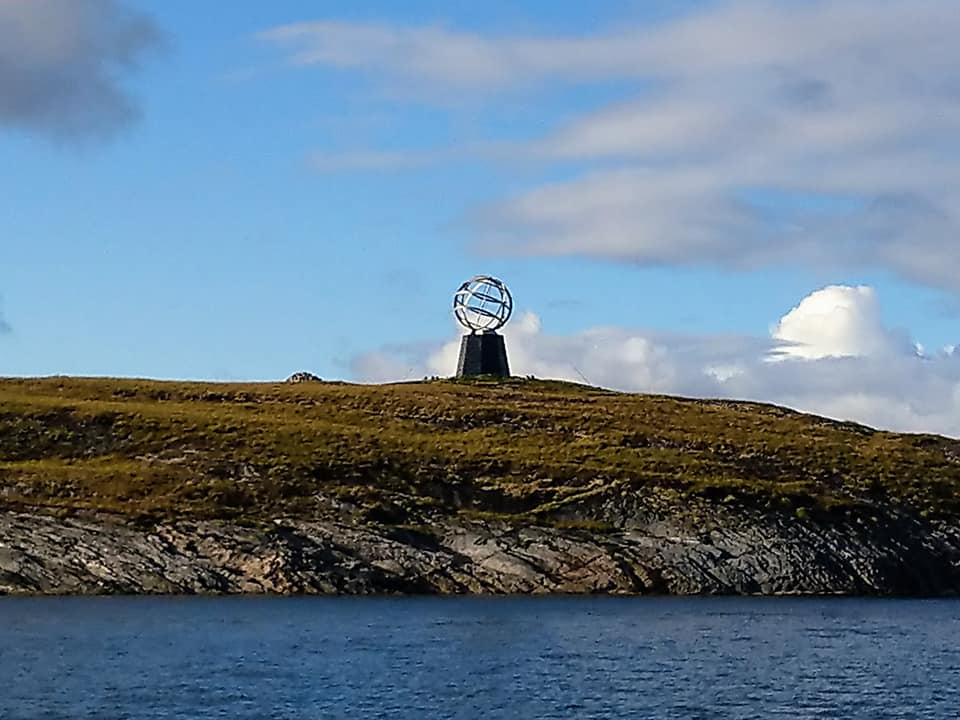 An Arctic Circle mark in Norway, sitting on a hill by the water.