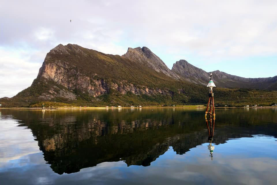 Extremely still waters reflecting a mountain and a guide post in the water. 