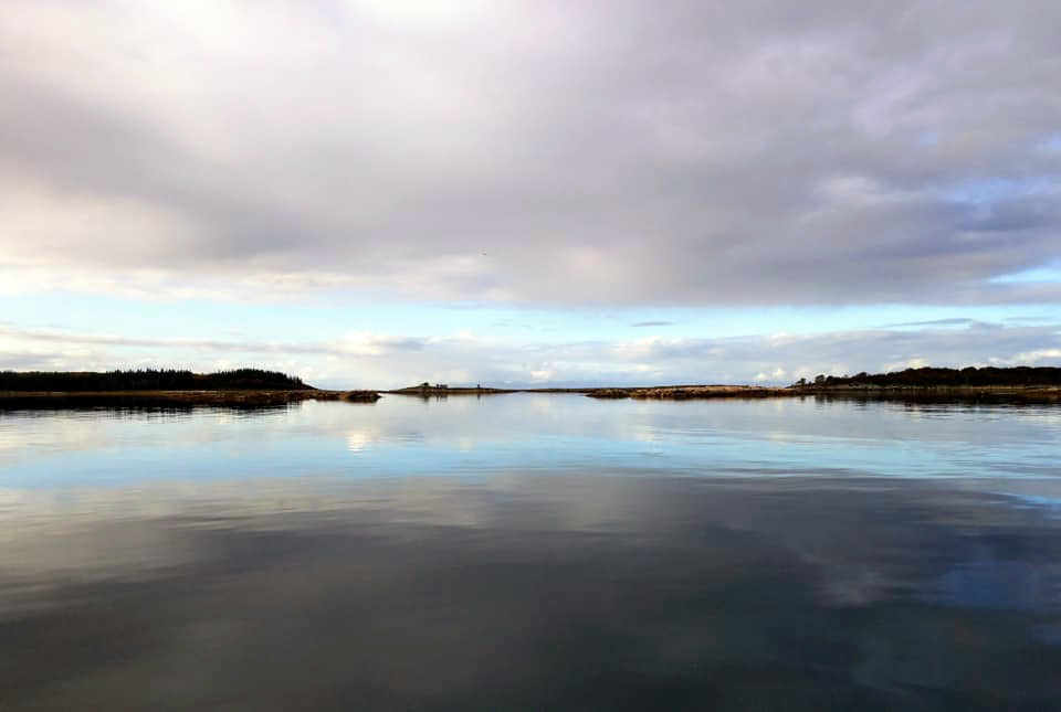 Very still waters and way in the distance a small glimpse of land. 