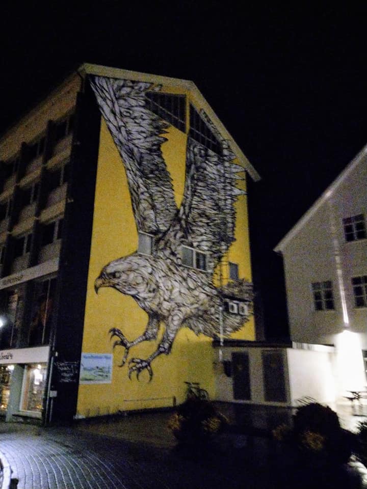 A murial on the end of a building, showing a huge white hawk on a yellow background.