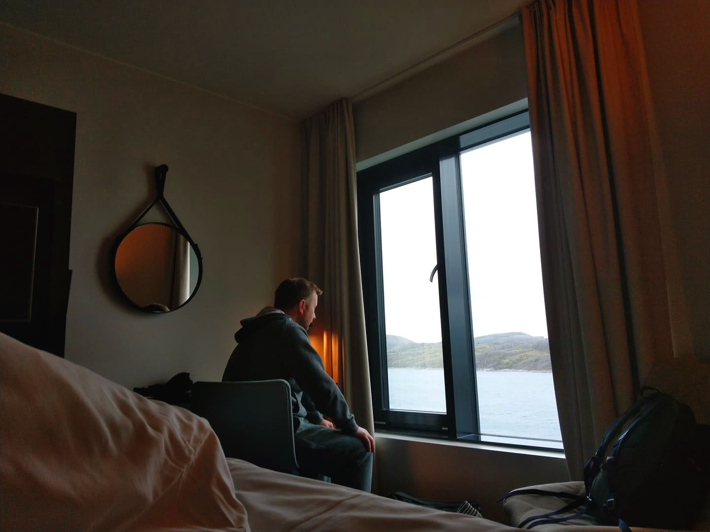 V sitting by a window in the hotel room looking out.