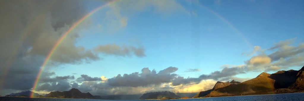 A huge double rainbow stretching over the sky and waters.