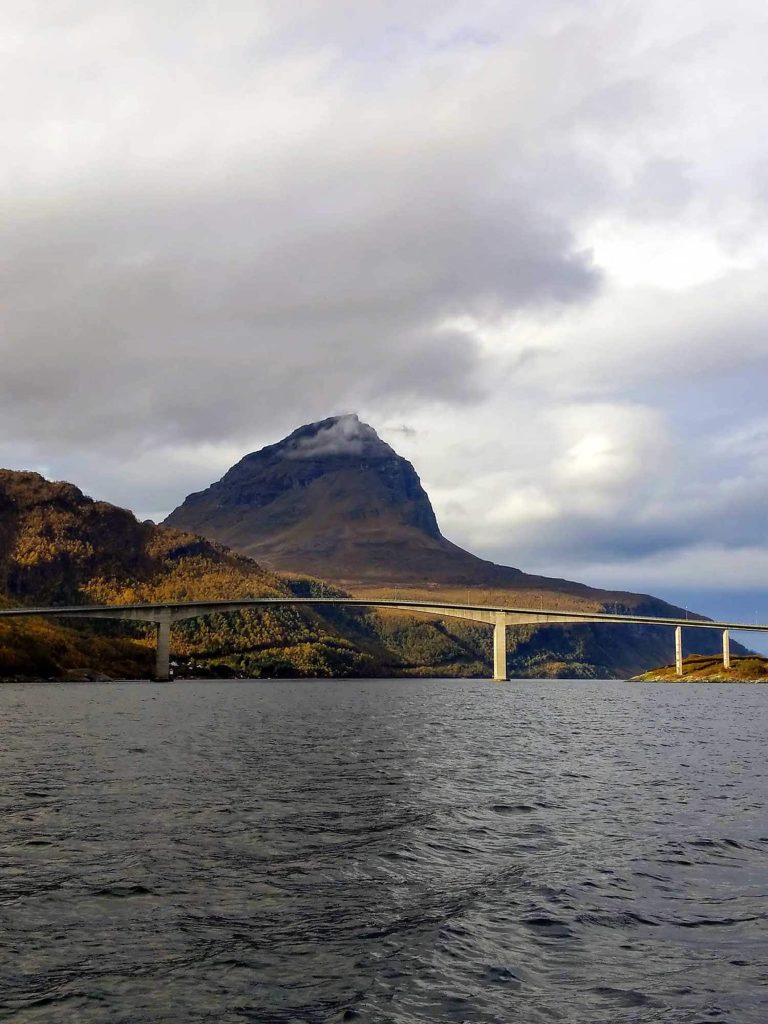 A big bridge going over water with a big mountain in the background.