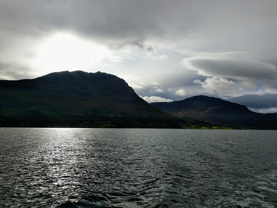 A silhouette of a mountain with the sun shining through the clouds in the background.