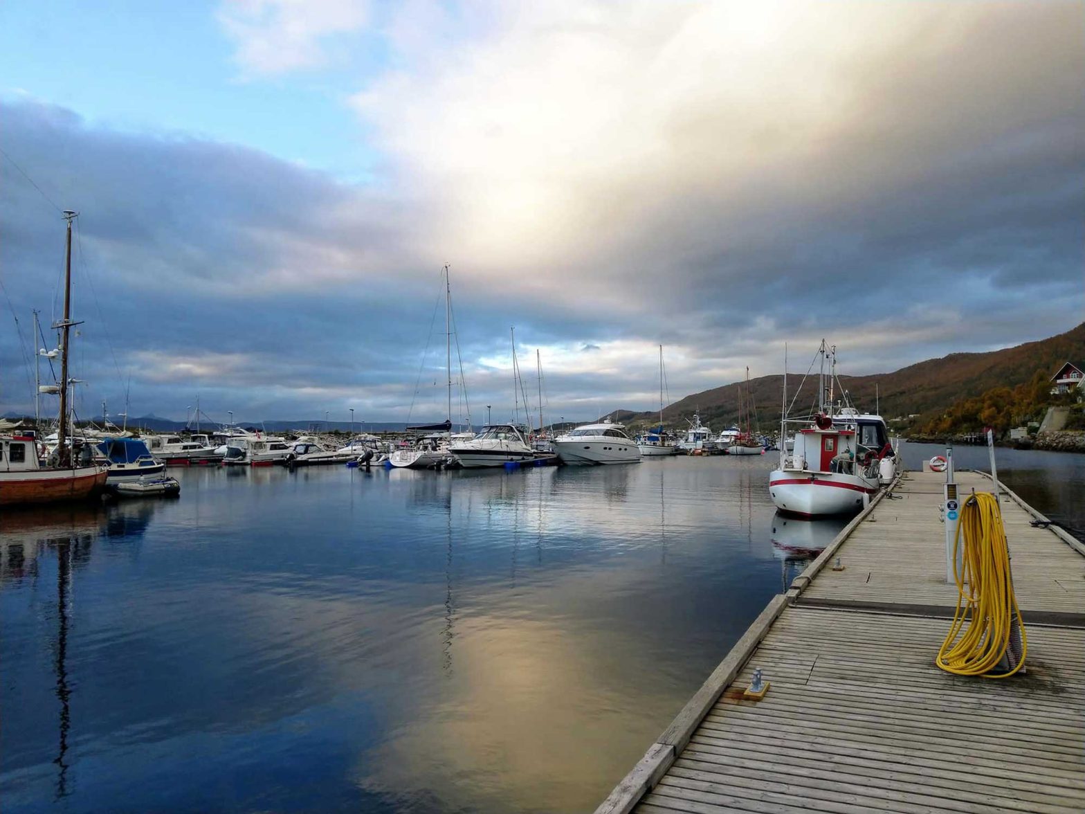 A marina full of boats with still waters reflective the clouds in the sky.