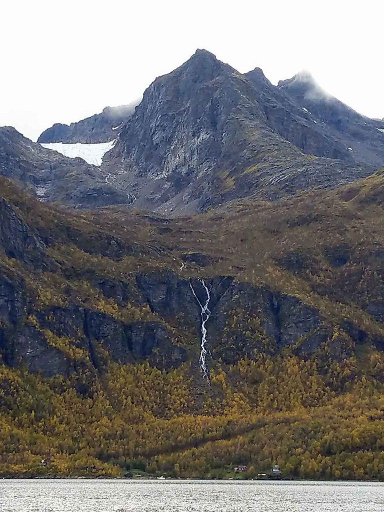 A mountain with a big waterfall running down, surrounded by trees changing colours for the fall season.