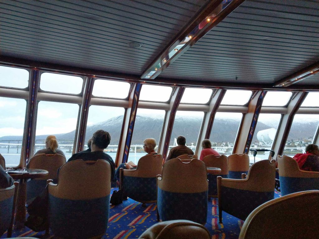 People sitting in chairs on the big ferry, Hurtigruten, looking out on the water.