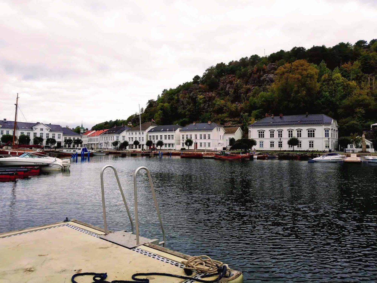 A view from the port in Risør overlooking the water and white houses with a forest in the background.