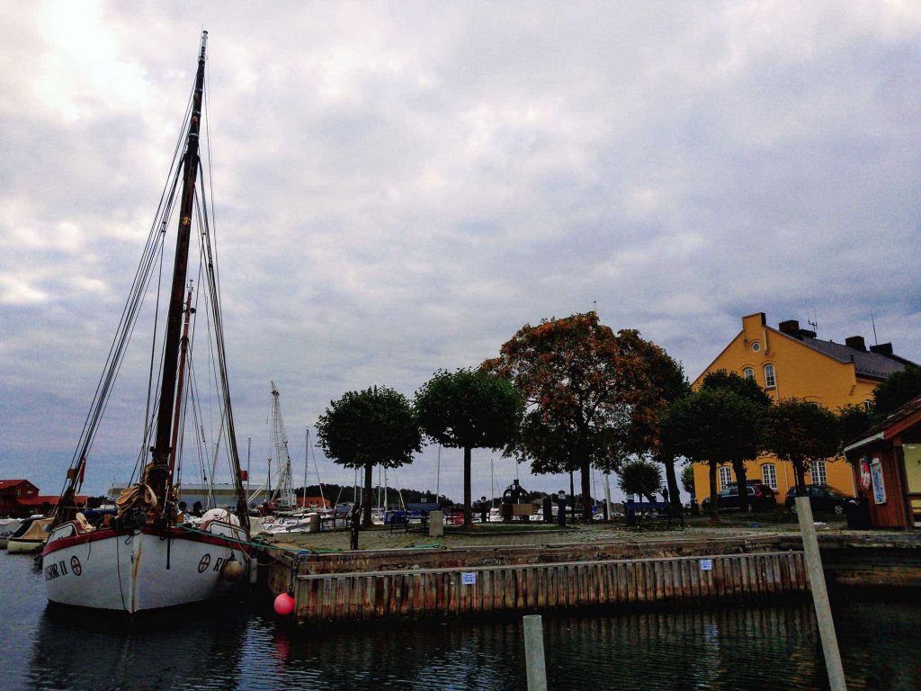 A sailboat by the docks, with a yellow house and trees.