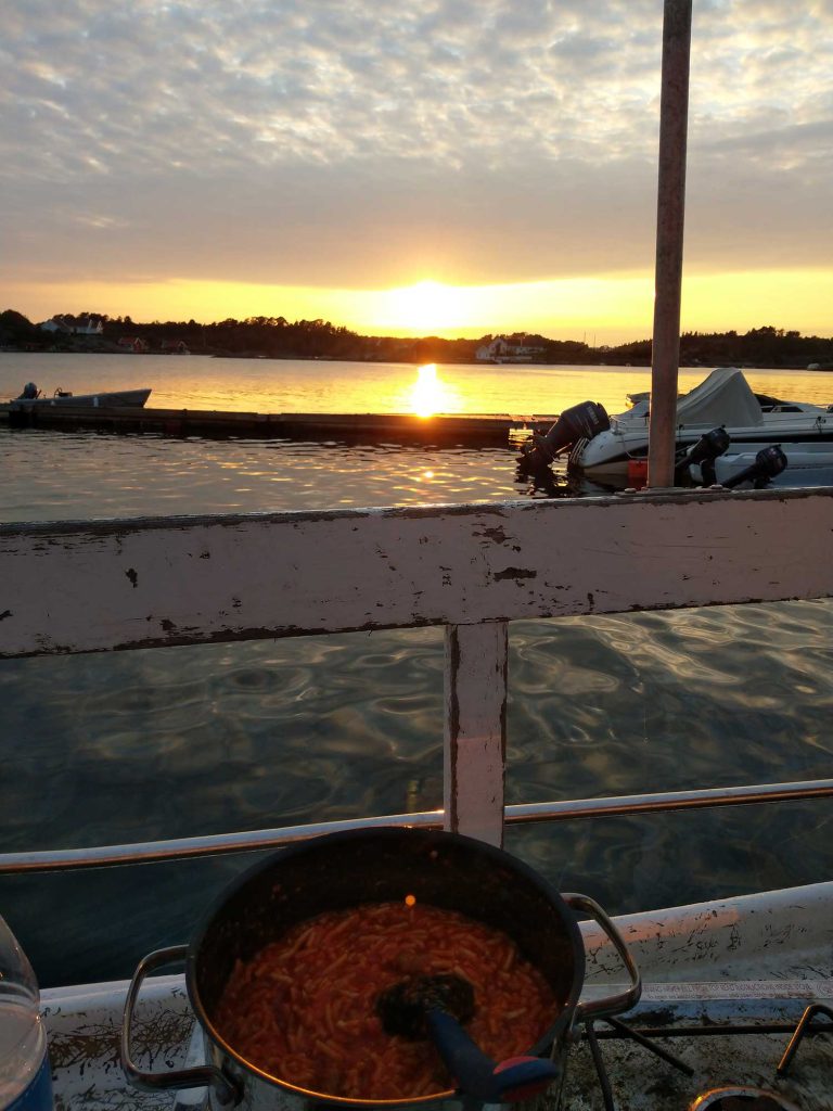 A view of the sunset from deck with a pot of food on the stove.