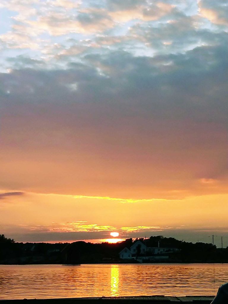 A yellow and pink sunset with calm water in the forefront.