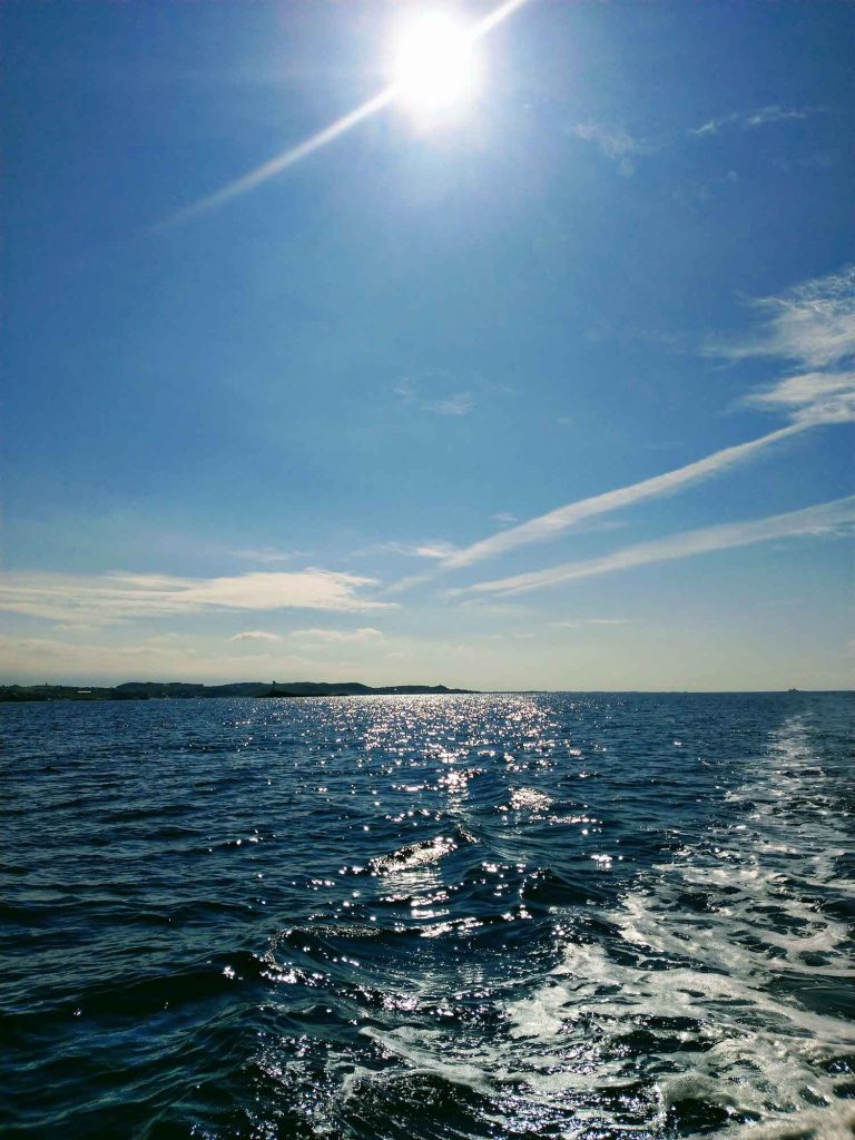 The sea and sky with the sun shining above and a few whispy clouds.