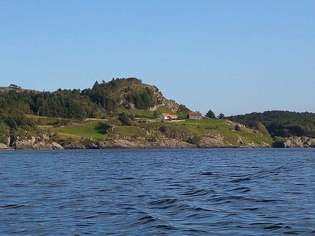 A house on a green hill by the water.