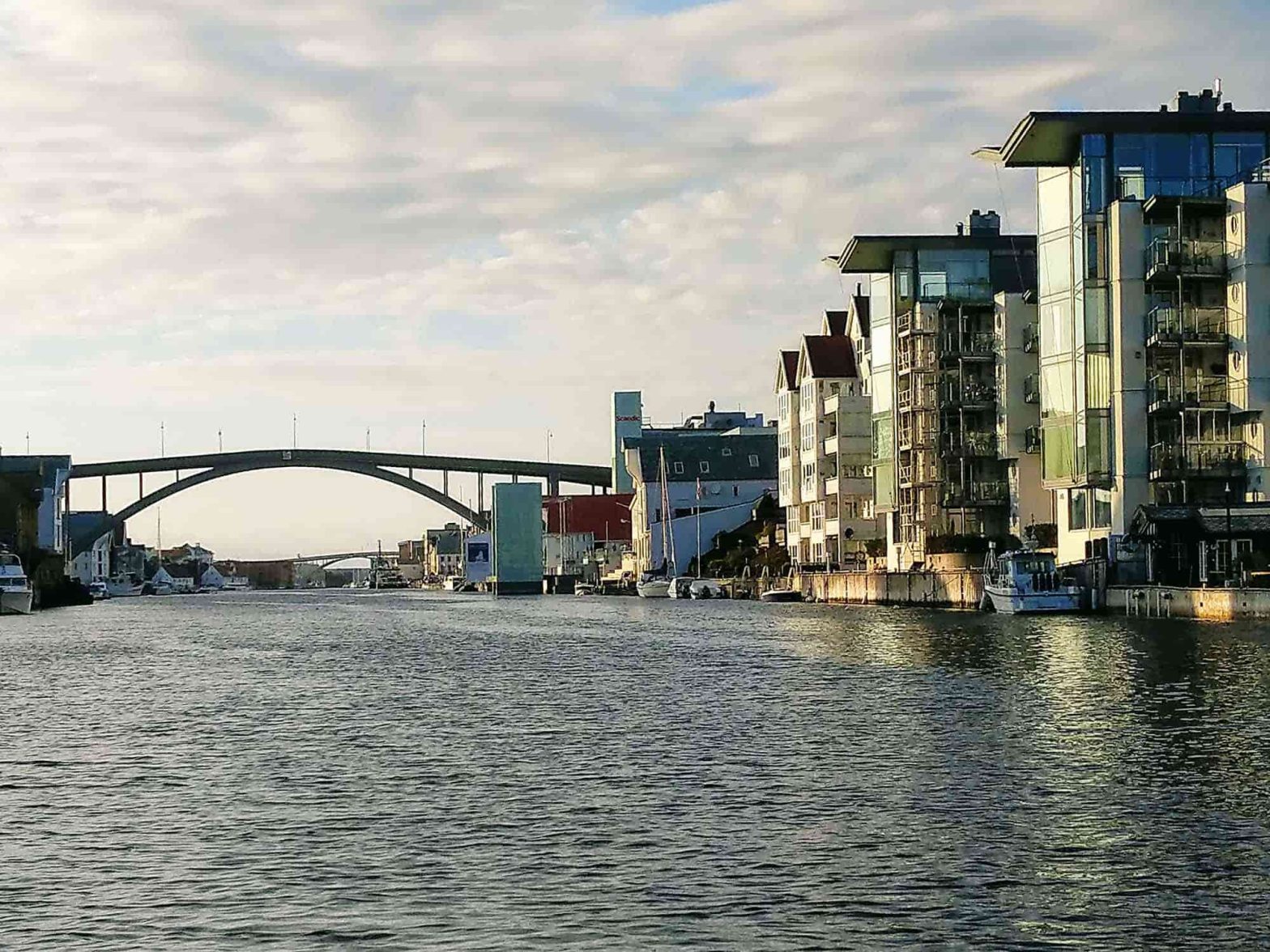 A view of Haugesund from the water. A bridge in the distance and apartment buildings along the shore on the right.