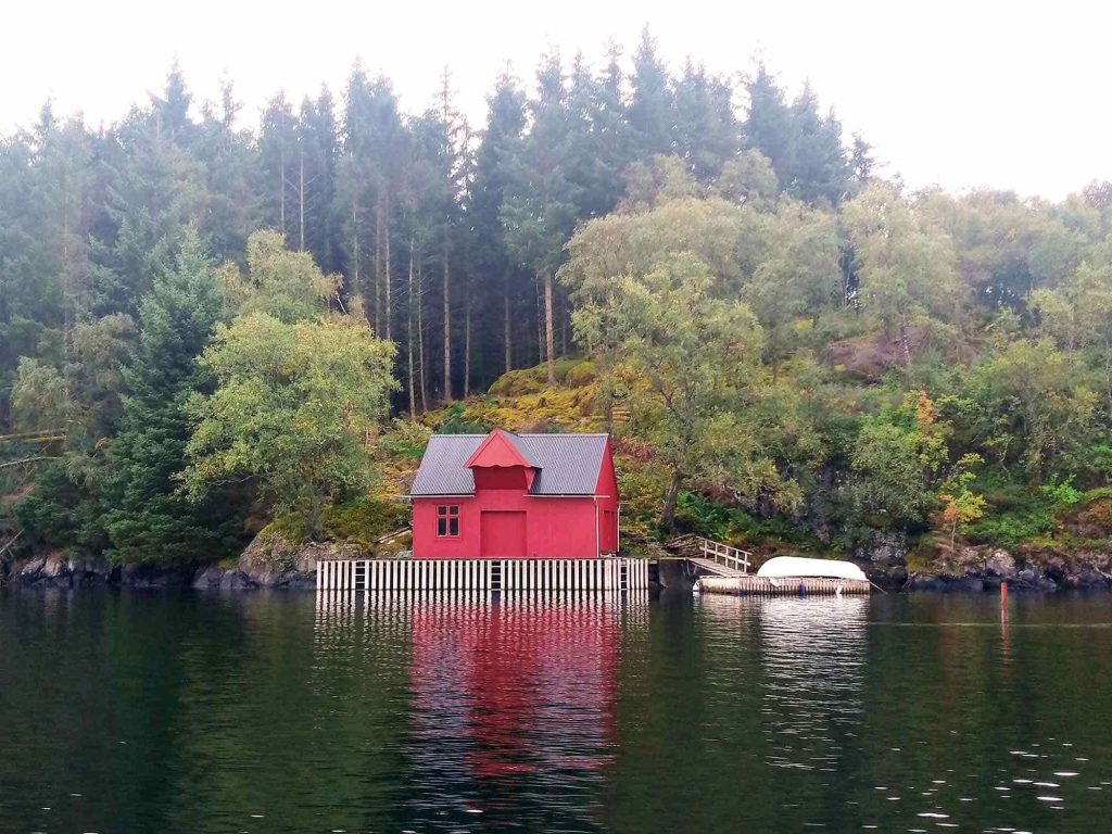 A small red boat house by the water and a forest in the background.