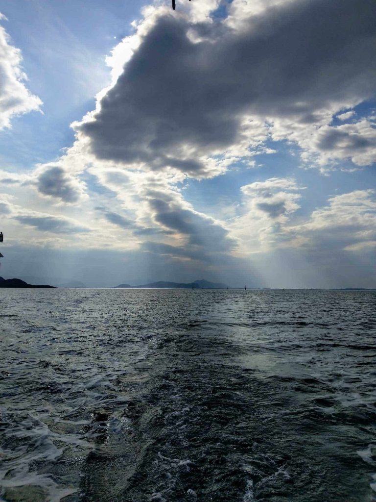 The ocean with dramatic clouds in the sky and the sun barely shining through.