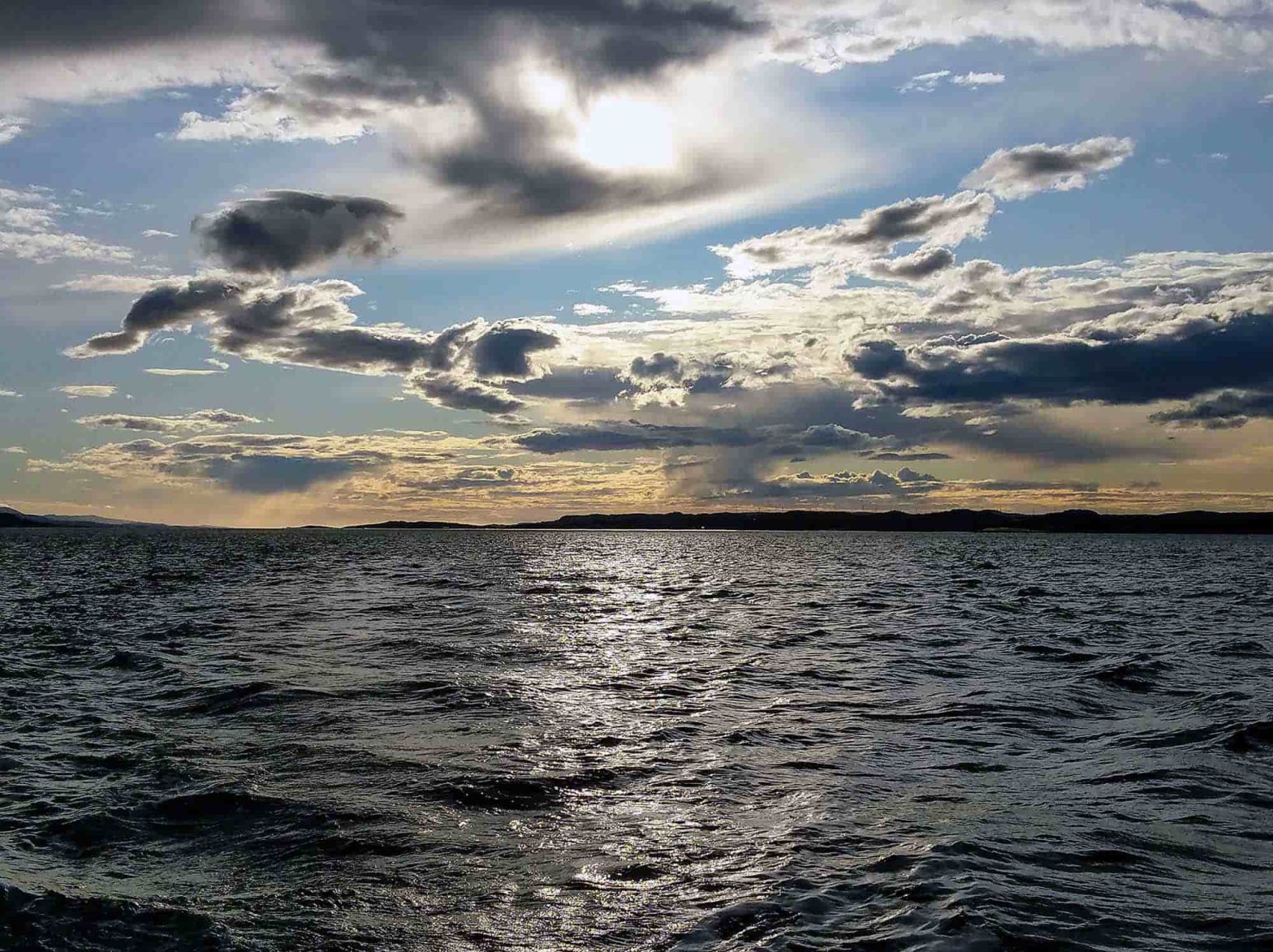 A shot of the ocean and a beautiful sky with whispy clouds and the sun shining through.