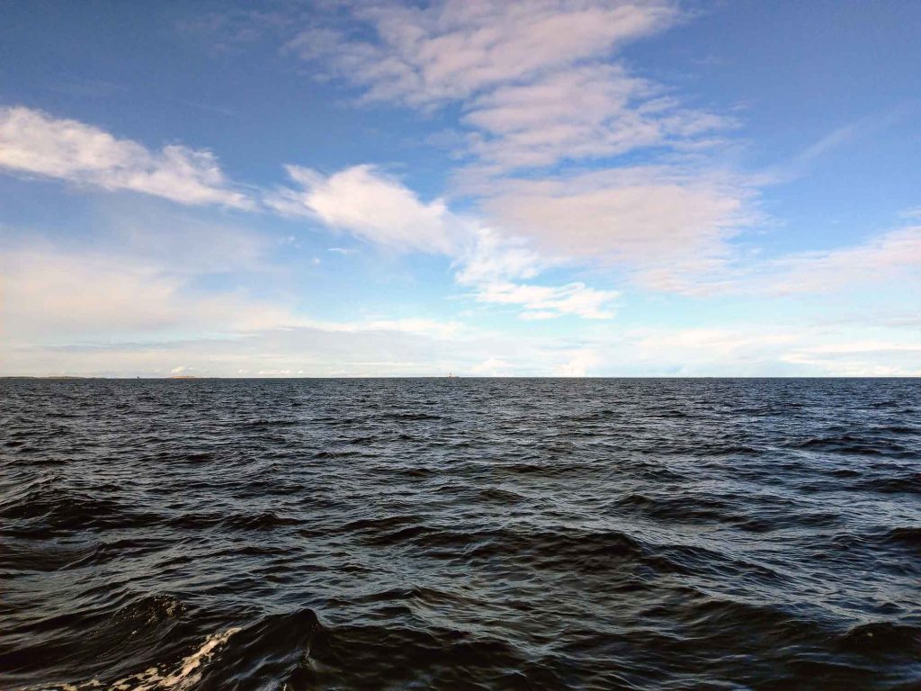 The dark sea and bright blue sky with a few clouds.