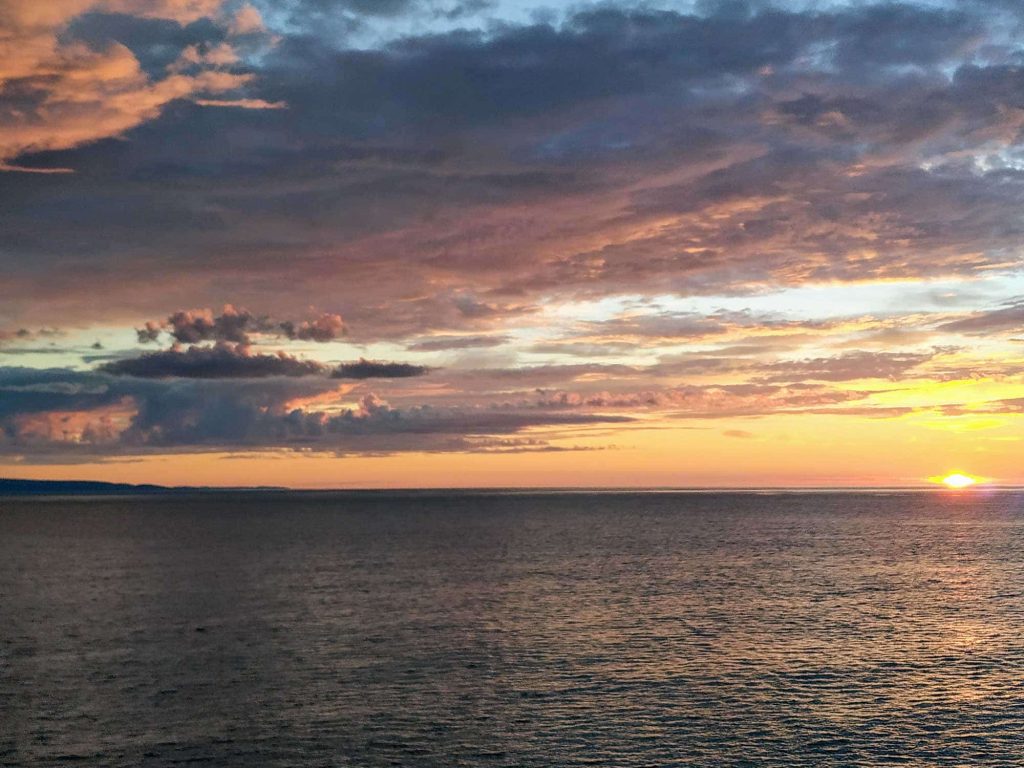 Big dramatic clouds over a sunset in the water.